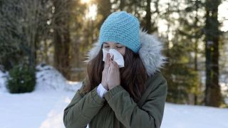 Junge Frau putzt sich die Nase draußen im winterlichen Wald (Quelle: imago/Westend61)