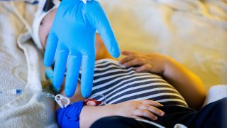 Ein aufgeblasener Handschuh hängt als Spielzeug vor einem achteinhalb Monate alten Kind, das mit einem Atemwegsinfekt auf der Intensivstation der Kinderklinik liegt und non-invasiv beatmet wird. (Quelle: dpa/Christoph Soeder)